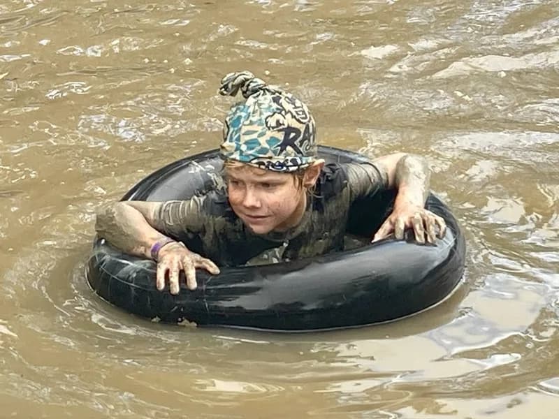 A child inside a tyre tube, floating in a muddy creek.