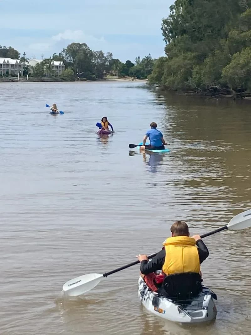 An occupational therapist and 3 children kayaking in a river.