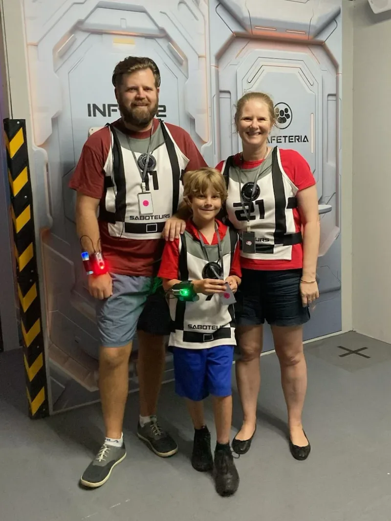 An occupational therapist, an adult, and a child, wearing activity vests while standing together for a photo.