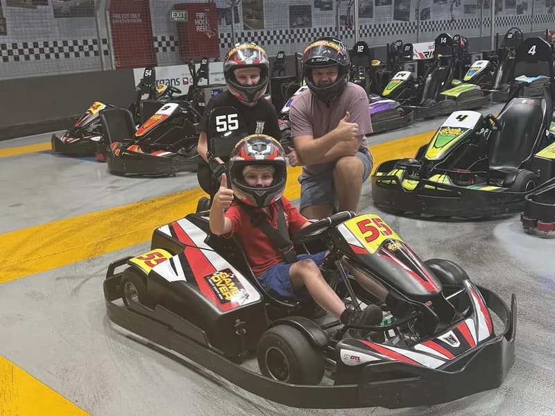An occupational therapist and child, kneeling behind another child sitting in a go-kart, looking at the viewer for a photo.