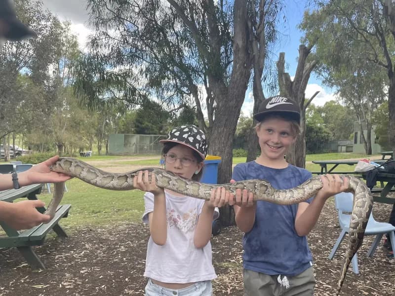 Two children, standing side-by-side outdoors, jointly holding and examining a large carpet python.
