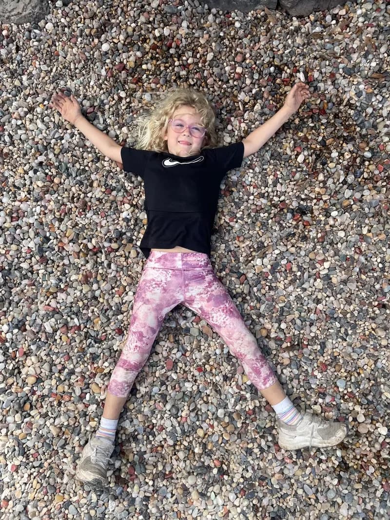 A child, performing a snow-angel, on a large pile of opals, while looking at the viewer and smiling.
