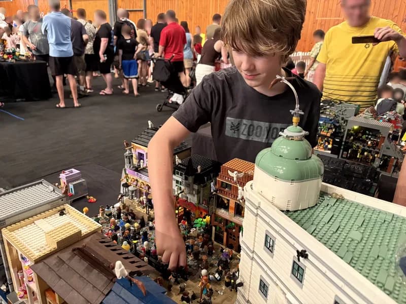 A child, looking at and playing with a large LEGO display, among a group of people.
